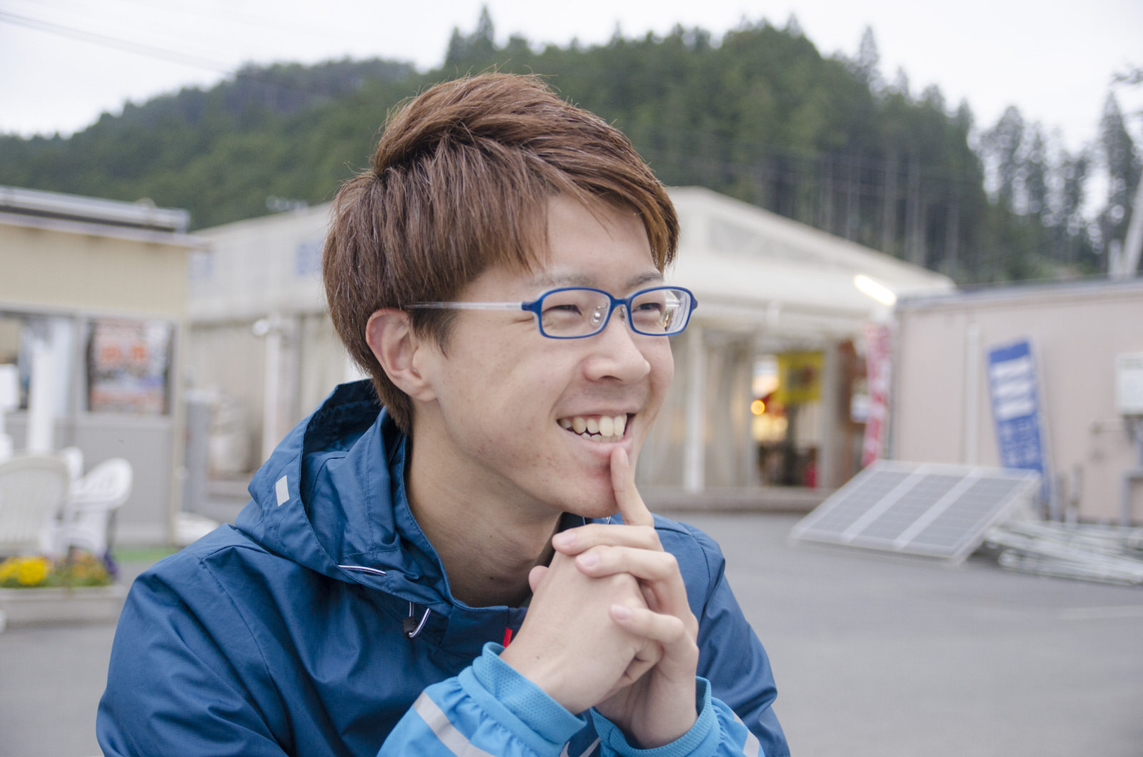 山のふもとに建つ店を背景に、笑顔の佐藤さんを写した写真