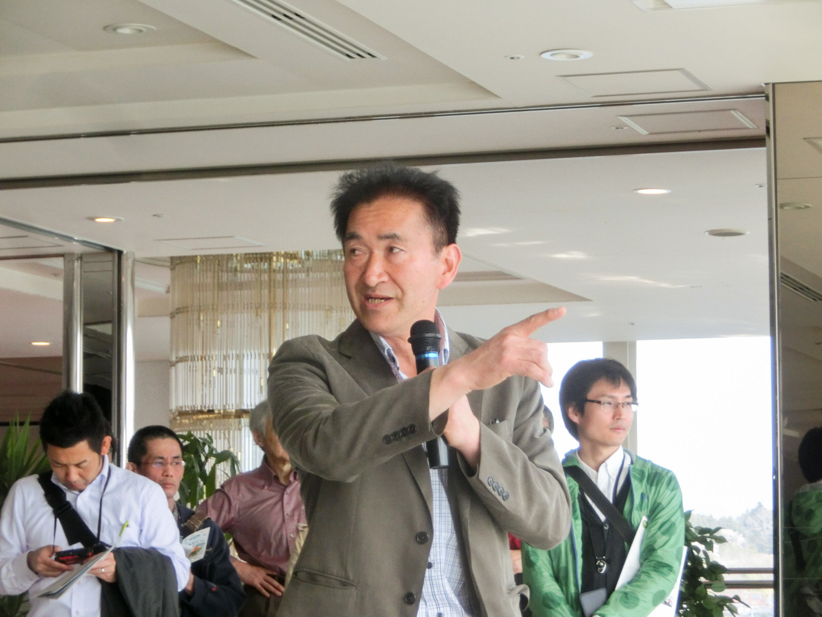 ホテルのロビーでマイクを持って左側を指さし話をしている後藤さんと、後ろで話を聞いている参加者たちの写真