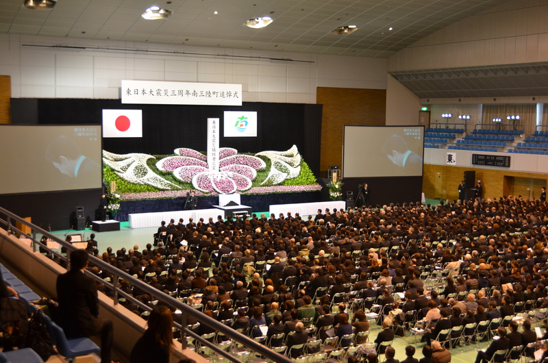 会場前方に慰霊碑ときれいな花で飾られた祭壇が設けられ、会場には多くの遺族の方々が席につき、参列している様子を写した東日本大震災南三陸町追悼式の写真