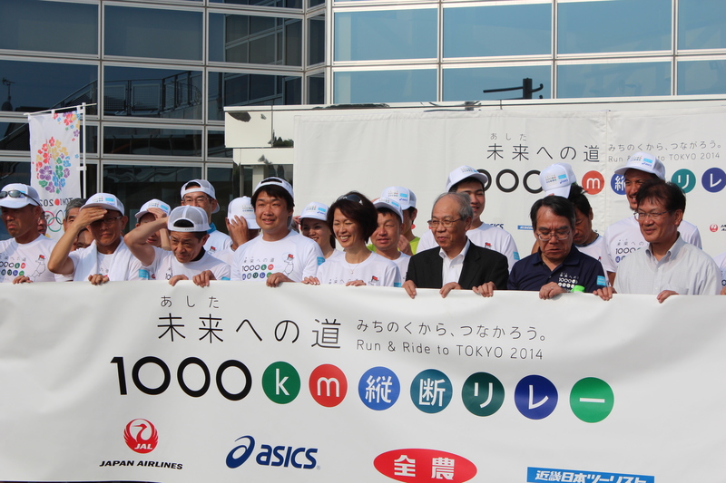 白いTシャツとキャップを着けた参加者たちが「未来への道1000km縦断リレー」と書かれた横断幕を手に並び、中央にゲストの有森裕子さんが笑顔で写っている写真