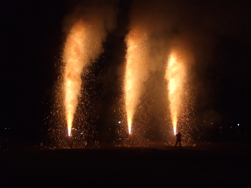 夜空の下、勢いよく3つのオレンジ色の火柱が立ち上がり、火の粉が舞い上がる八幡川かがり火まつりの様子の写真