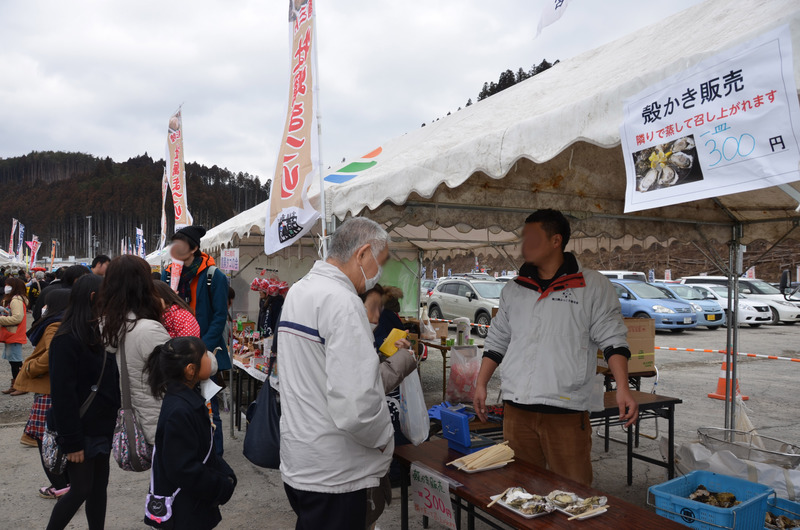 志津川湾牡蠣まつり福興市の会場で、テントの下に設けられた販売コーナーに「殻かき販売」の掲示とのぼり旗が立ち、多くの来場者が店の前に並んでにぎわっている様子の写真