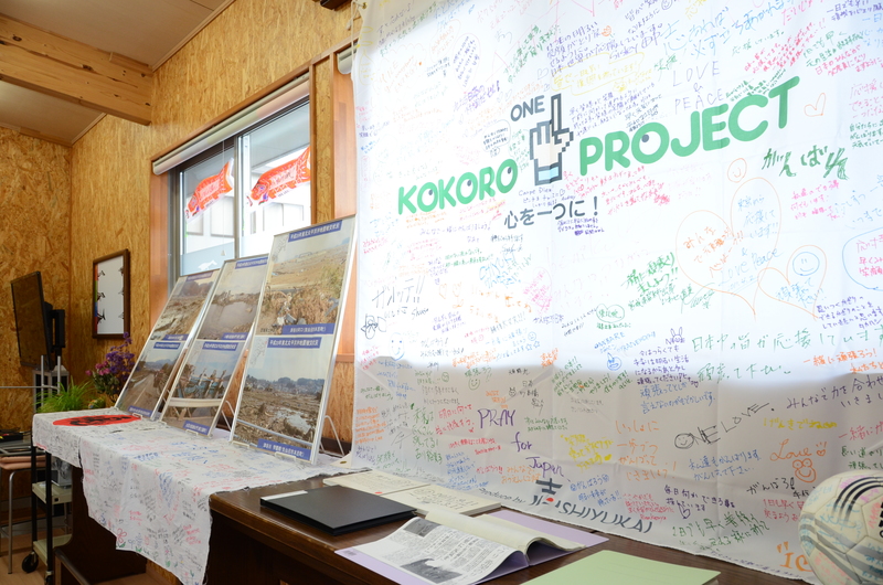 室内に、「KOKORO PROJECT」と書かれた寄せ書きの大きな横断幕や震災当時の写真パネルが並び、多くの人の思いが感じられる東日本大震災展の様子の写真