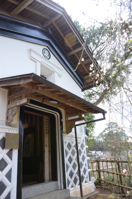 白壁に黒いなまこ壁が美しい伝統的な土蔵造りの建物で、木の門構えと瓦屋根が風格を漂わせる松笠屋敷の写真