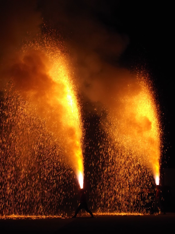 夜空に向かって勢いよく火花を噴き上げる2本の手筒花火を、人々が力強く構えている迫力ある写真