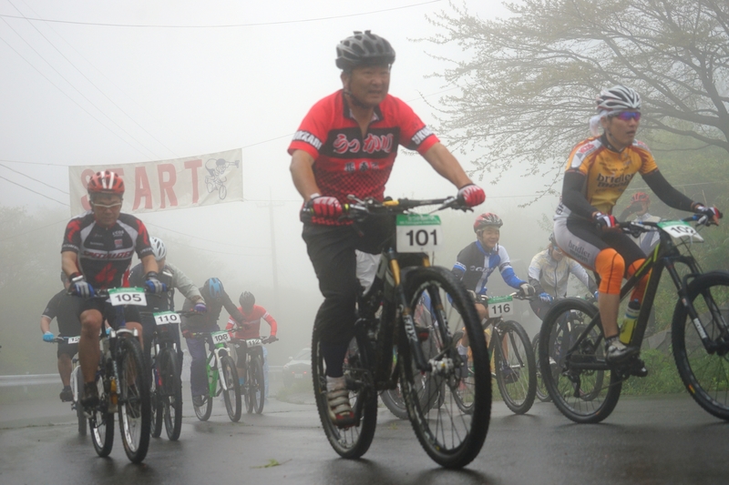 霧の中、スタート地点を自転車で元気に走り出す参加者たちの写真