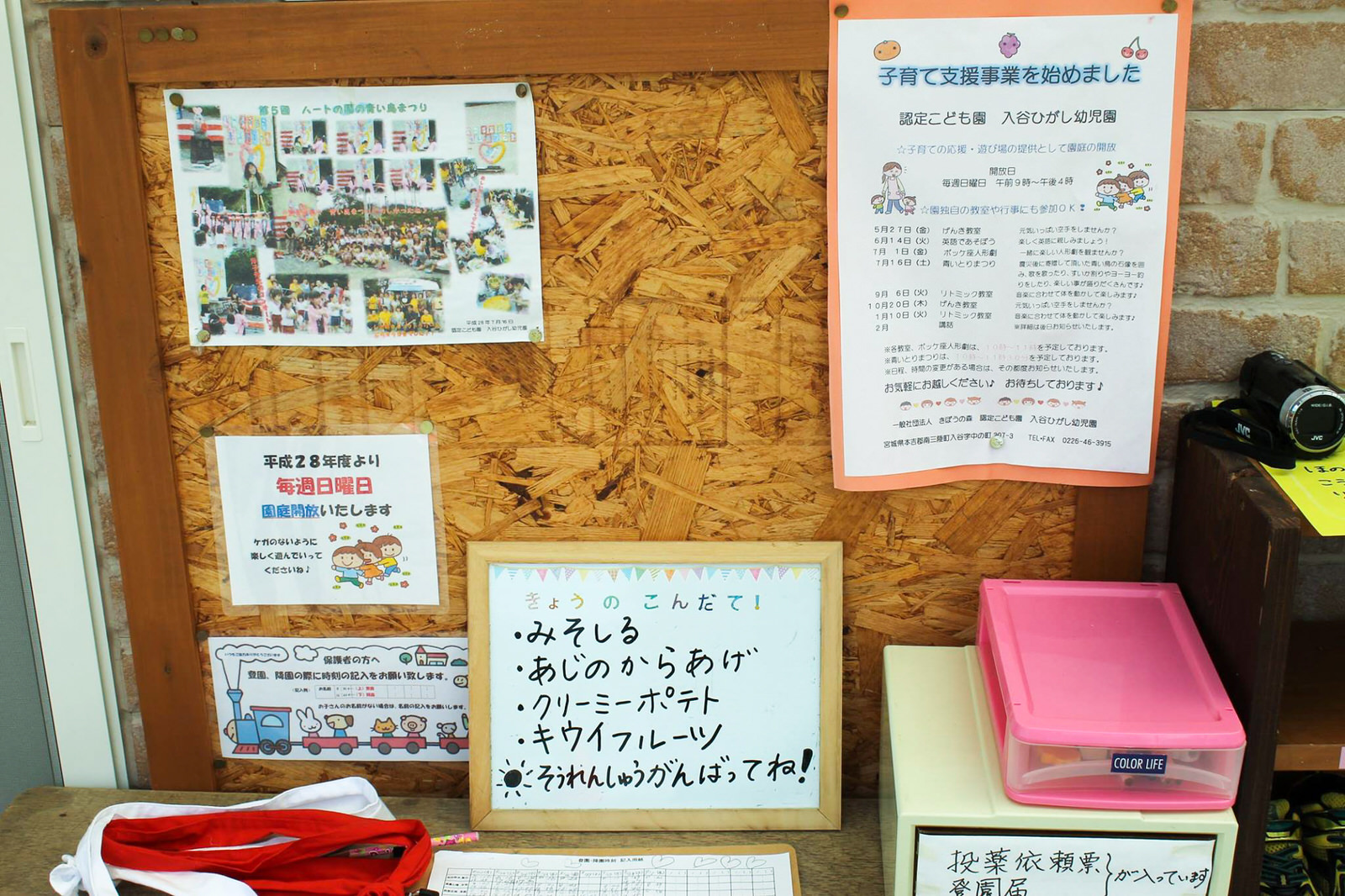 投薬依頼書の収納箱などが置かれている掲示板に、行事の写真や給食の献立表、「子育て支援事業を始めました」と書かれた案内、休園日のお知らせなどが掲示されている写真