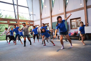 室内の広い部屋で青い服を着た子どもたちが、右手右足を前に出し、左足を引き左手を斜め上に上げてよさこいの練習をしている写真