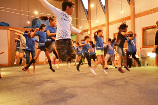 室内で青い服の子どもたちがジャンプしている瞬間をとらえたよさこいの練習の写真