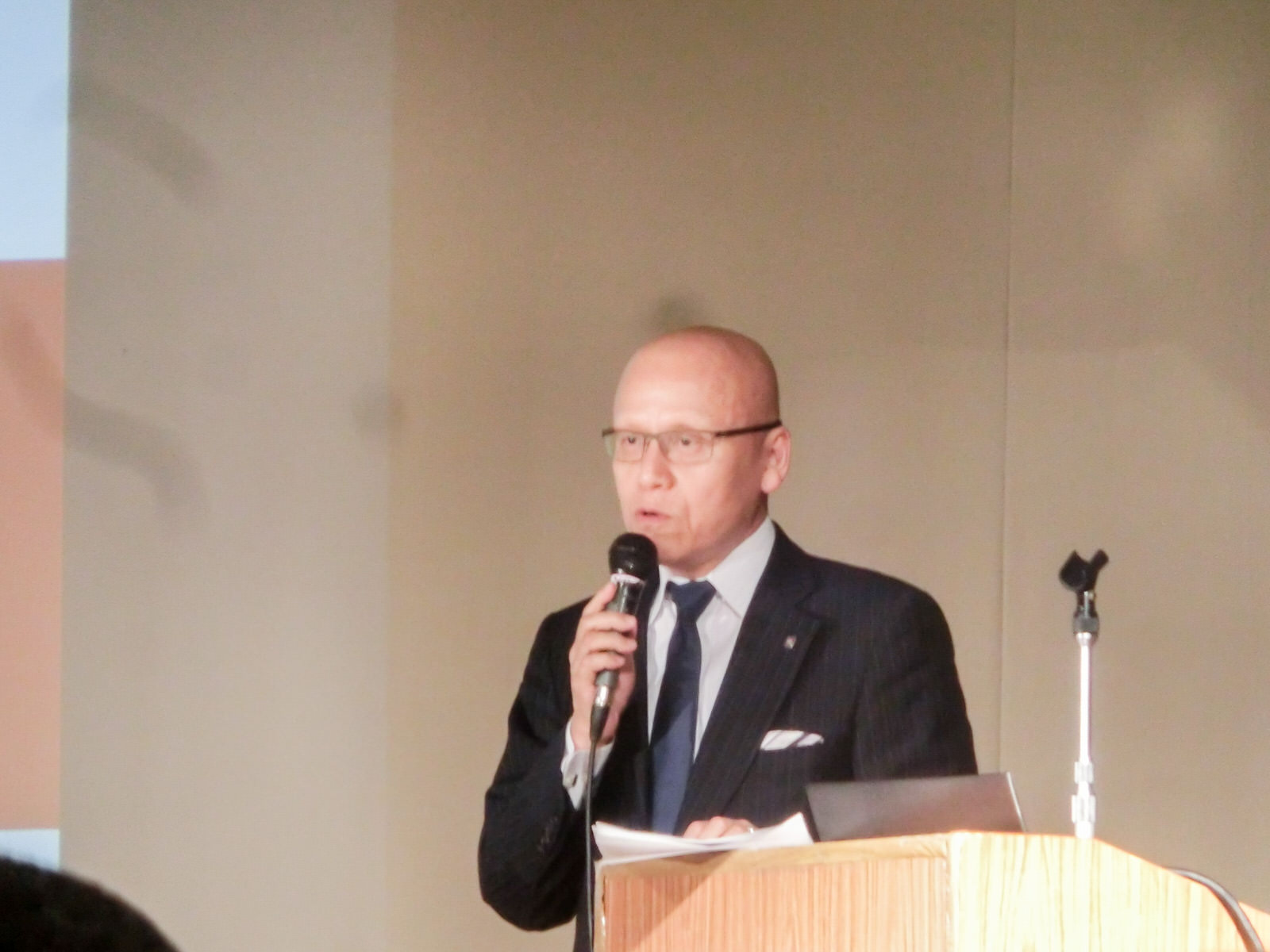 演台の横に立った熊野 英介氏が、マイクを持って客席の方を見ながら話をしている写真