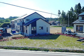 白と黒の新築住宅の前に芝生と花が整えられ、隣に建設中の住宅やトラックが見える住宅地の写真