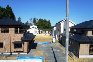 両側に黒い瓦屋根の二階建て住宅が建ち、奥に更地が続く造成中の住宅地の写真