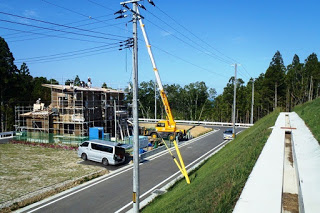 左側で木造住宅の建築工事が進められ、クレーン車や作業車が停まっている開発途中の宅地の写真