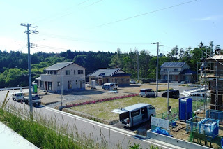 複数の戸建て住宅が建ち並び、空き区画には工事車両や仮設トイレが設置された新しい住宅地の写真
