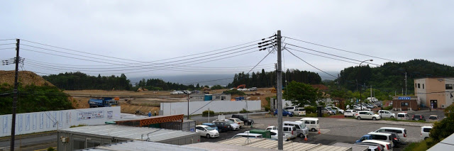 広い駐車場と道路と白いフェンスで隔てられた先に土の平地が広がっている写真