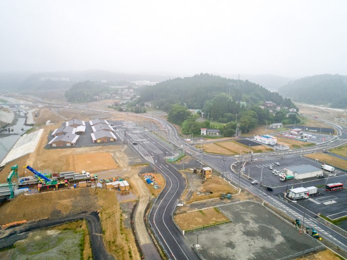 霧が立ち込める山々に囲まれた町で、道路工事が行われている様子を上空から捉えた、静けさと活動が同居する風景の写真