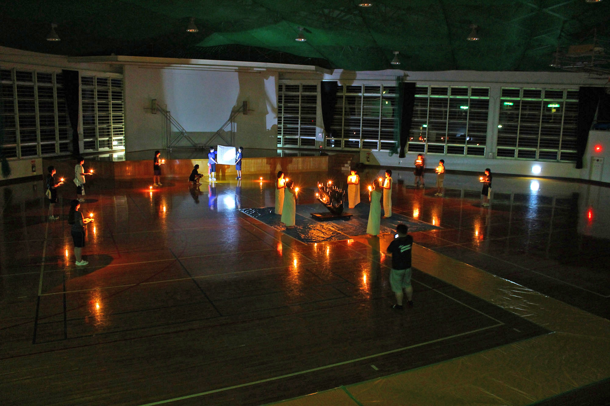 広く薄暗い体育館のような場所で、等間隔に広がったジュニアリーダーたちがそれぞれ手にキャンドルを持ちキャンドルセレモニーが行われている様子の写真