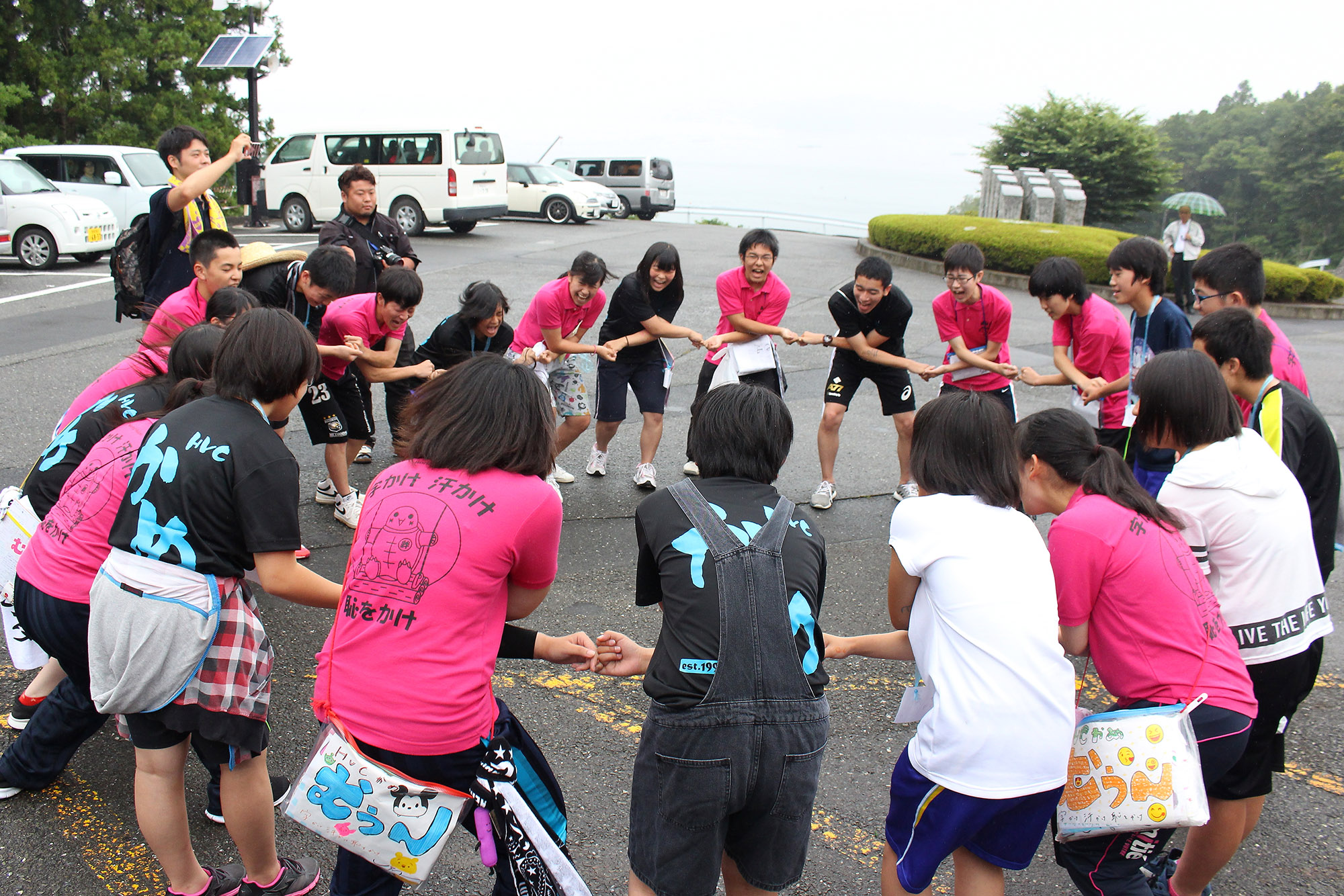 参加したジュニアリーダーたちが、体の前でクロスした手を横の人とつなぎ、1つの大きな輪を作っている写真