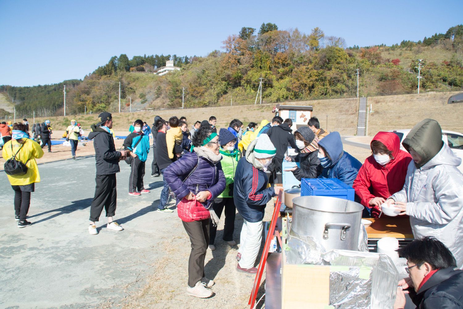 大きな鍋が置かれたブースに沢山の参加者が並んでいる写真