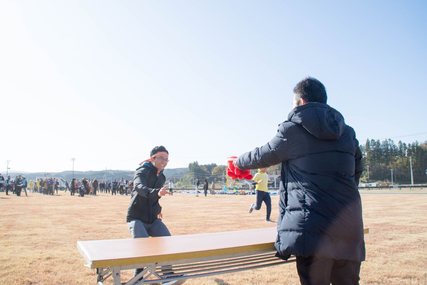 黄色いくちばしの付いた白い鳥の被り物をかぶったメンバーが、手をつないでリレーを行っている様子と、 長机のそばでタコの「オクトパス君」を左手に持つ男性と、鉢巻きを巻いた男性が笑顔で右手を伸ばしている「オクトパス君リレー」の一場面を写した写真