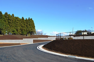 カーブしている舗装された新しい道路の奥に、土が盛られた宅地の区画が並ぶ造成地の写真