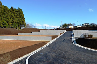 真っ直ぐ伸びる坂道の舗装道路の左右に段々のように区画された宅地が並ぶ造成中の住宅地の写真