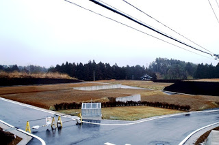 雨で舗装道路が濡れていて、区画された宅地にまだ家が建っていない造成地の写真