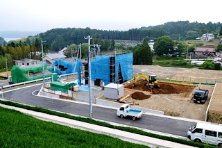 青いネットで囲まれた住宅が建設中で、重機やトラックが作業している新しい分譲地の写真