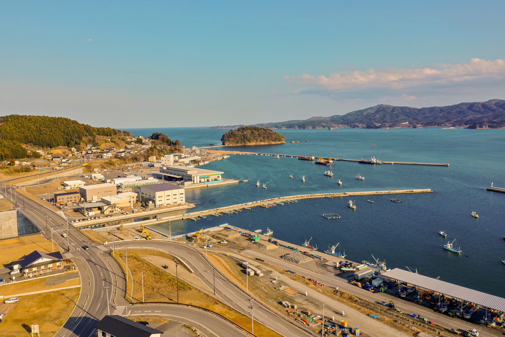海沿いの町にある港とその周辺の建物や道路、海に浮かぶ船などを上空から広く見渡すように撮影した写真