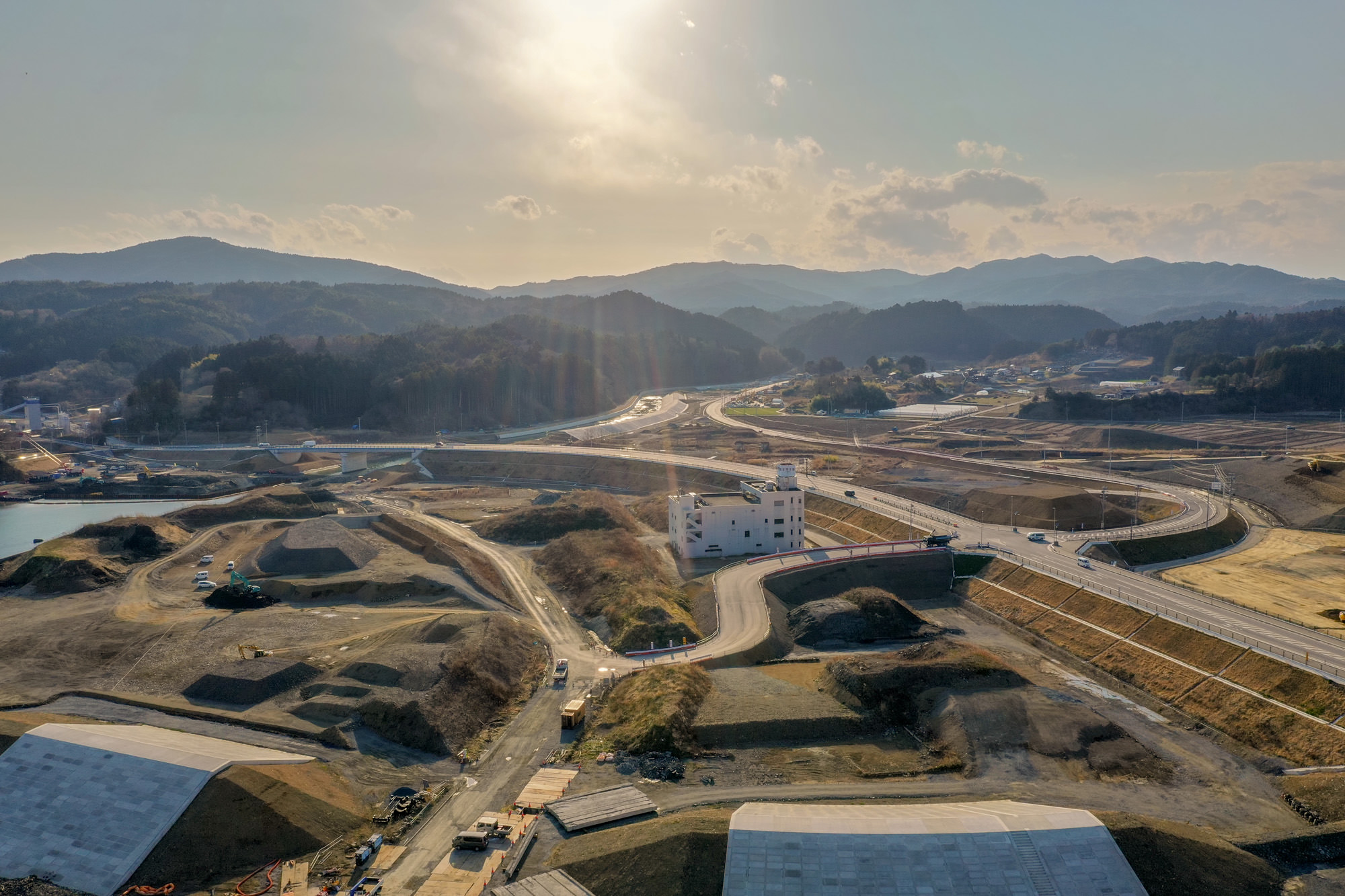 山々に囲まれた広い土地に道路や建物が点在し、自然と人の営みが混在する様子を上空から撮影した山間地域の写真