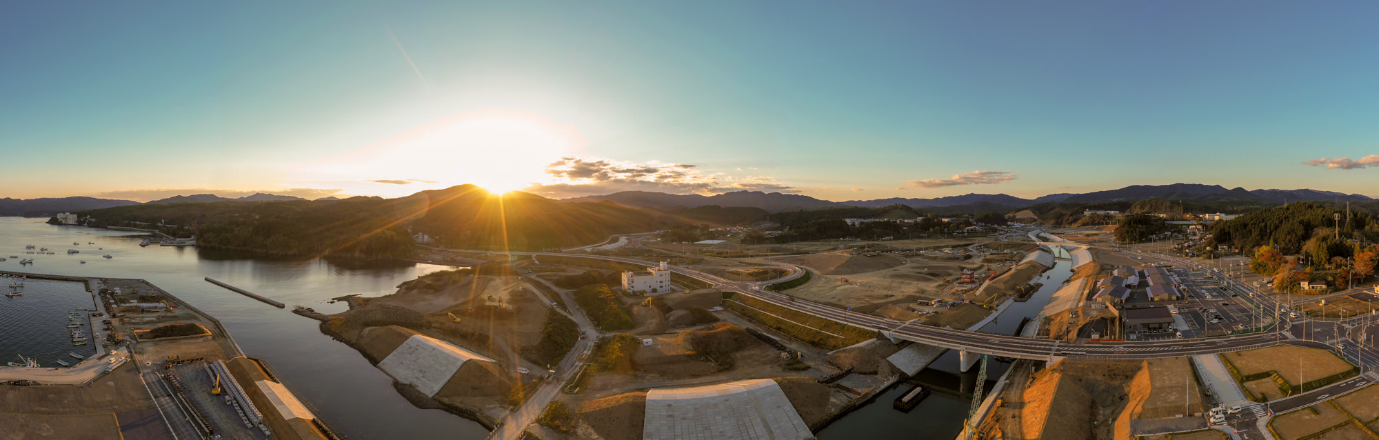 夕日が山々の向こうに沈みかけており、その光が静かな川面に反射して周囲の自然を柔らかく照らしている風景の写真