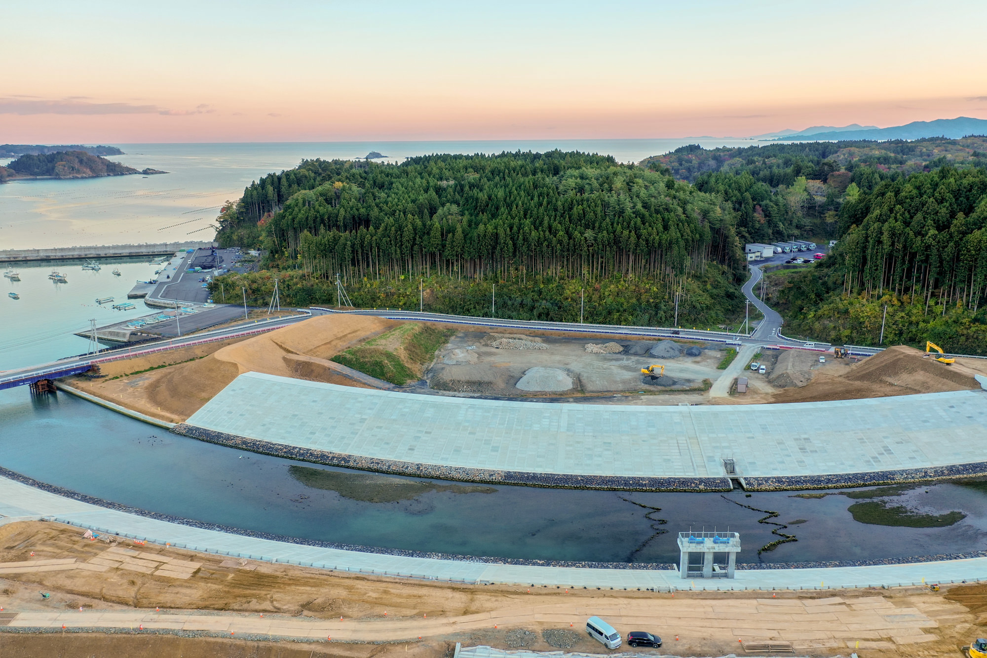 海岸沿いに長く伸びる防波堤が建設されており、その背後には緑豊かな森林が広がっていて、自然と人工構造物が共存する様子が見える写真