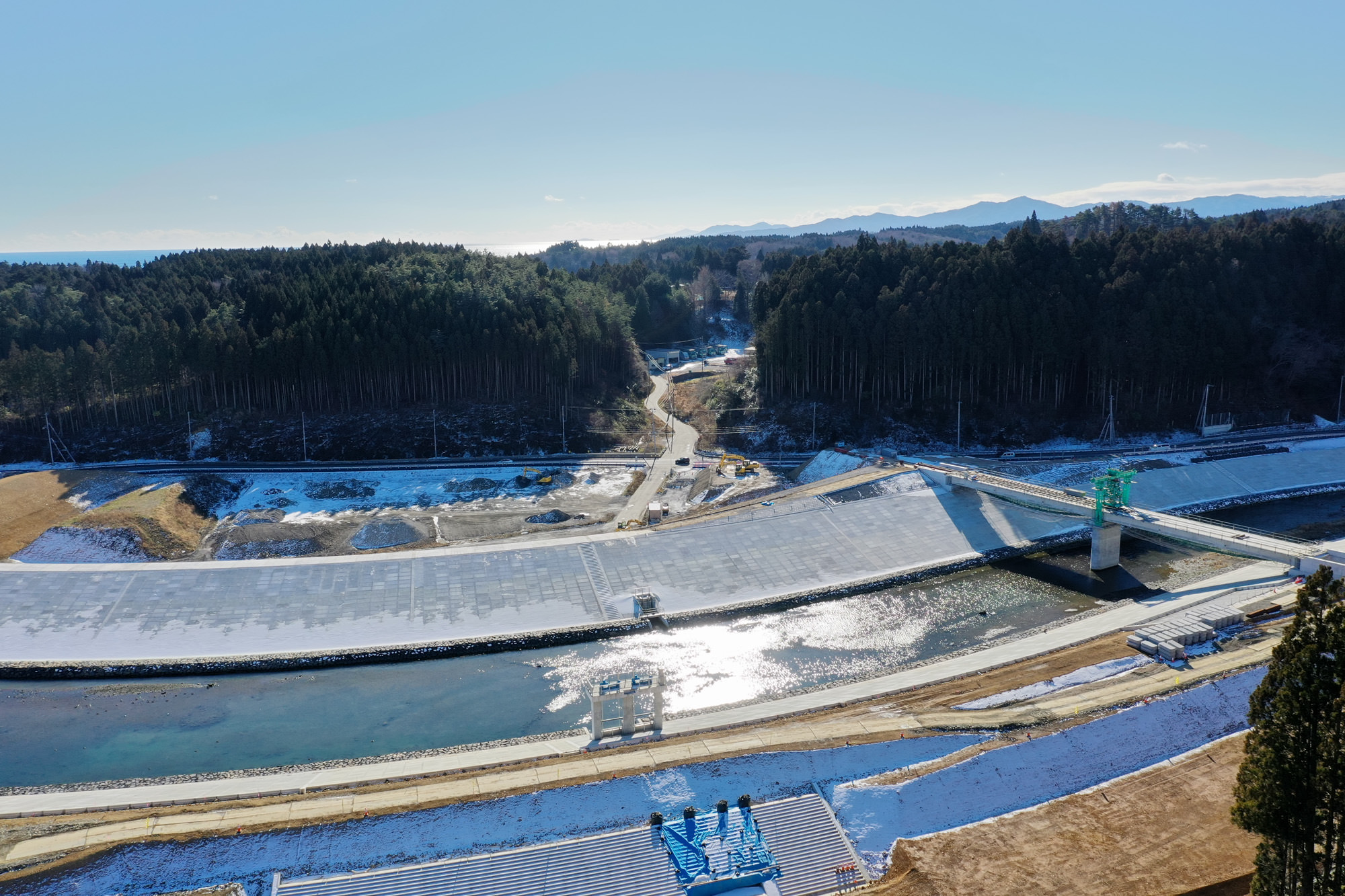 水が流れる川の堤防が舗装され奥には森林と山々が連なっている静かな自然の中の構造物の写真
