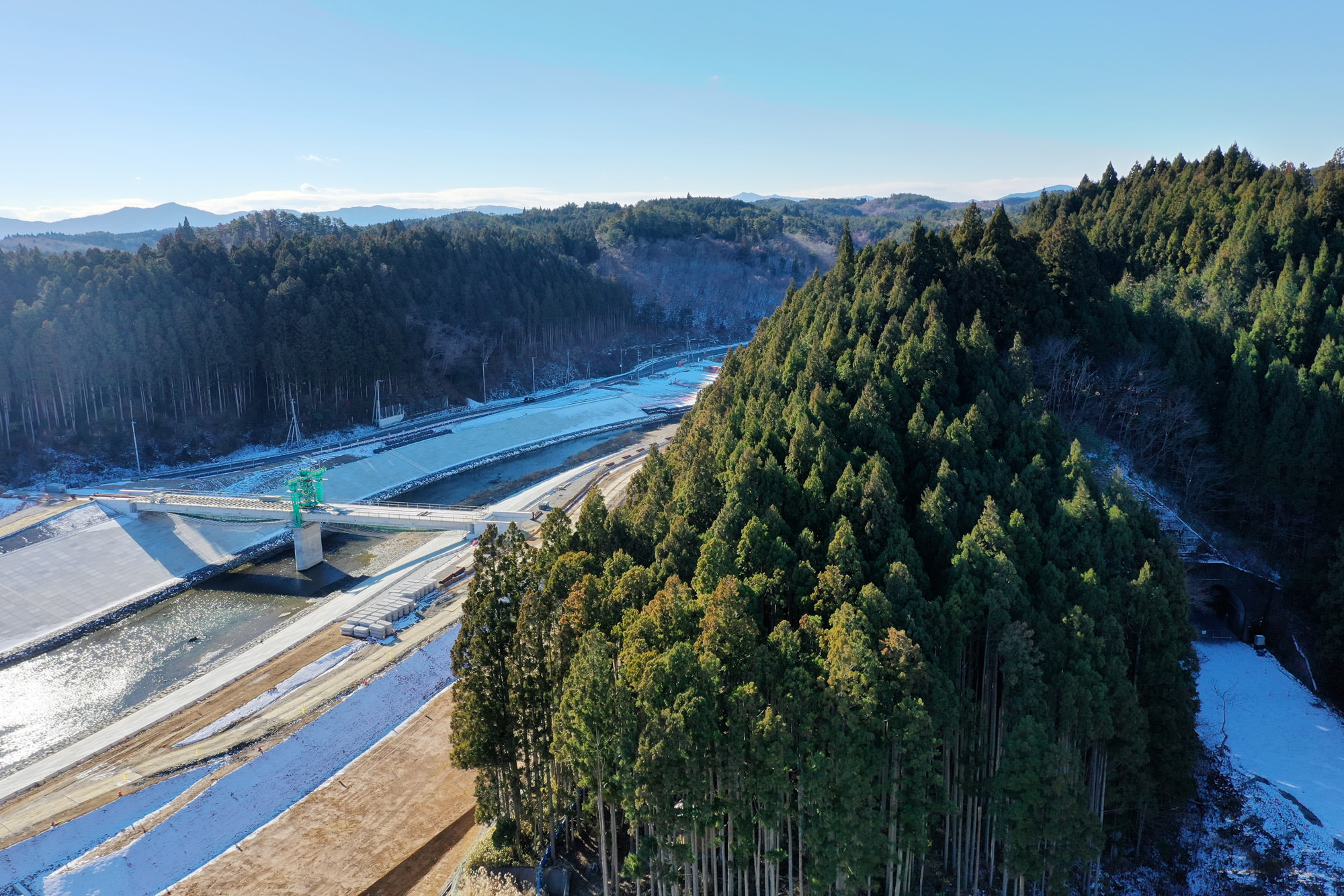 山間部に位置する川沿いに広がる森林の中にダムが設けられており、自然の地形に沿って水が流れ、周囲には木々が密集している風景の写真