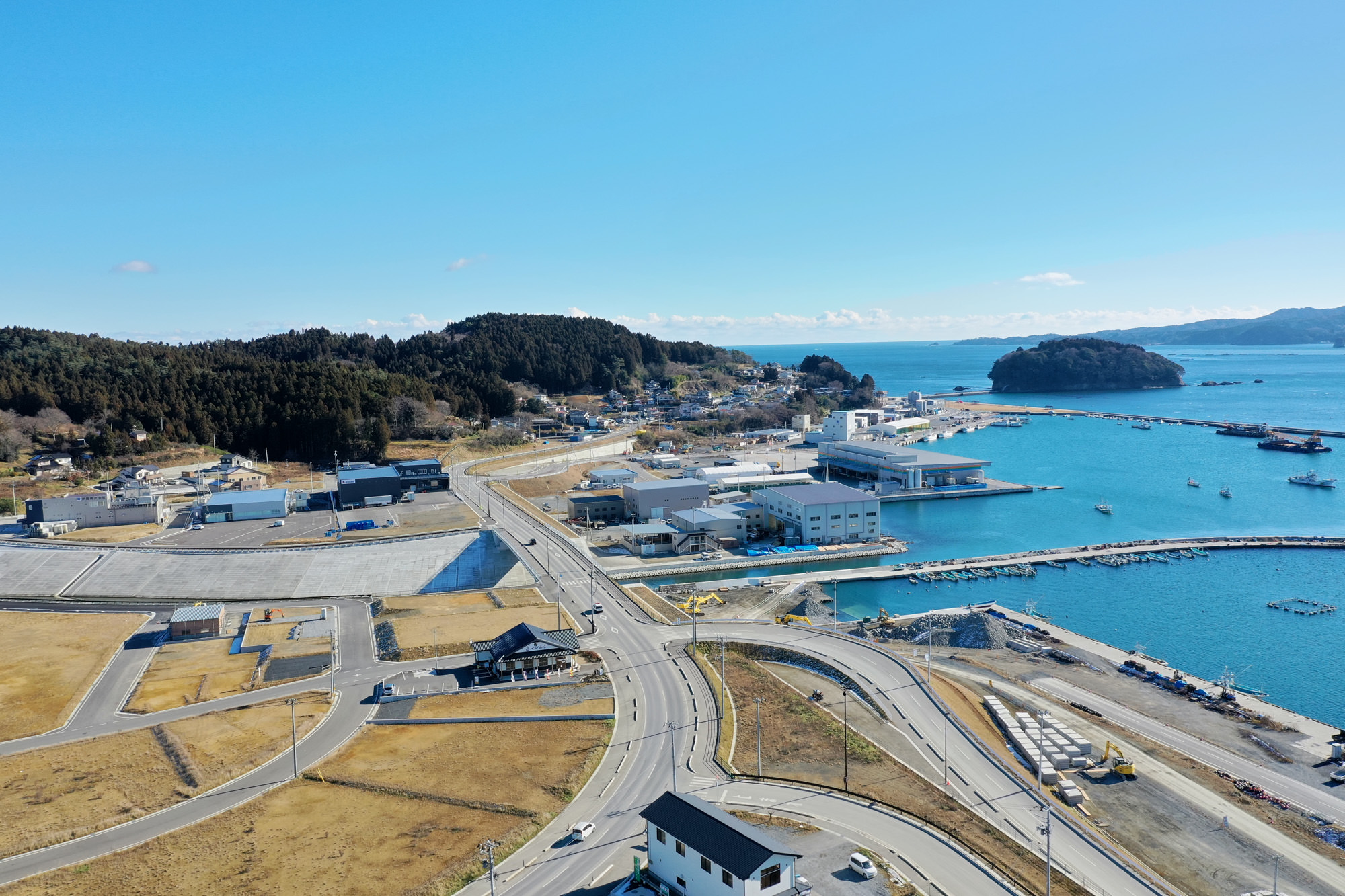 海に面した町で、複数の建物や道路、港の設備が整備されており、海岸沿いには船や桟橋が並び、背景には木々に覆われた丘と沿岸に点在する建物が見える漁業や海運が盛んな地域の風景の写真