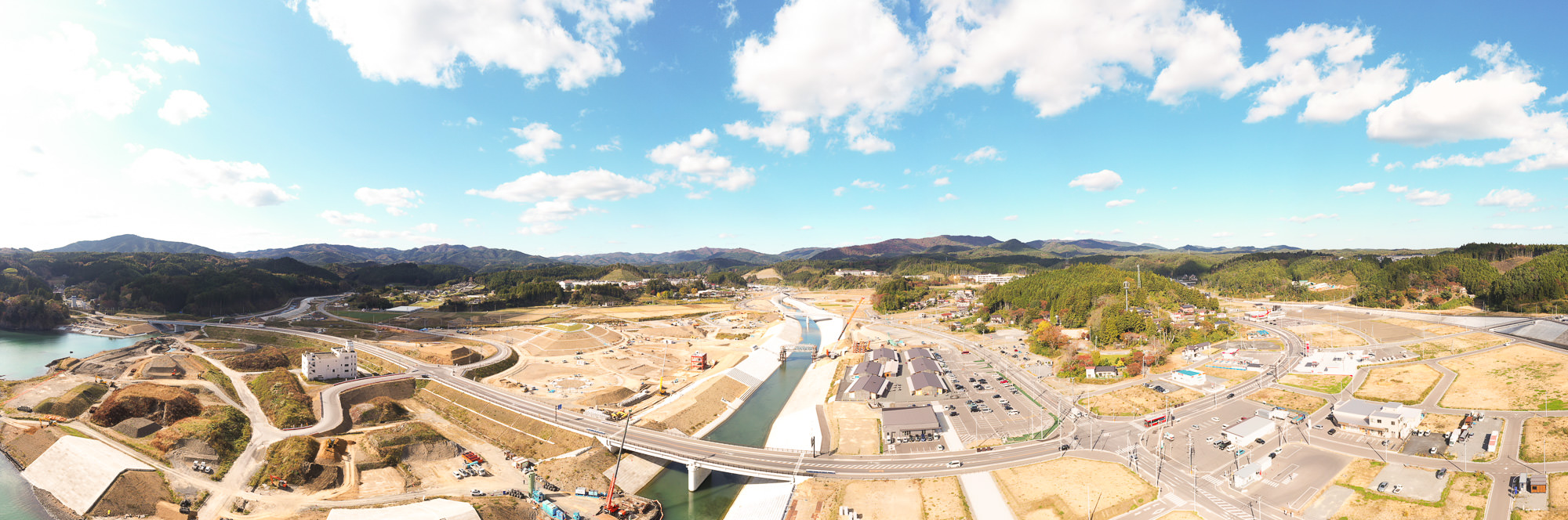 中央にカーブした道路があり奥に山並みが見える白い雲が浮かんだパノラマの風景写真