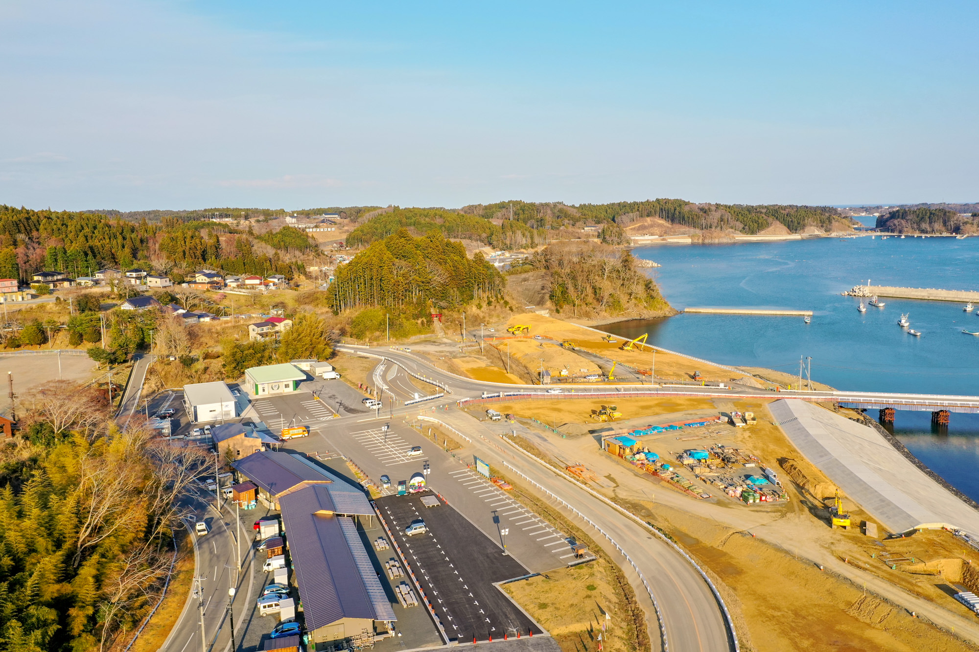 海沿いの町を空から撮影しており、道路や駐車場、建物が並び、工事現場も確認できる町の様子を広く捉えた海辺の町の写真
