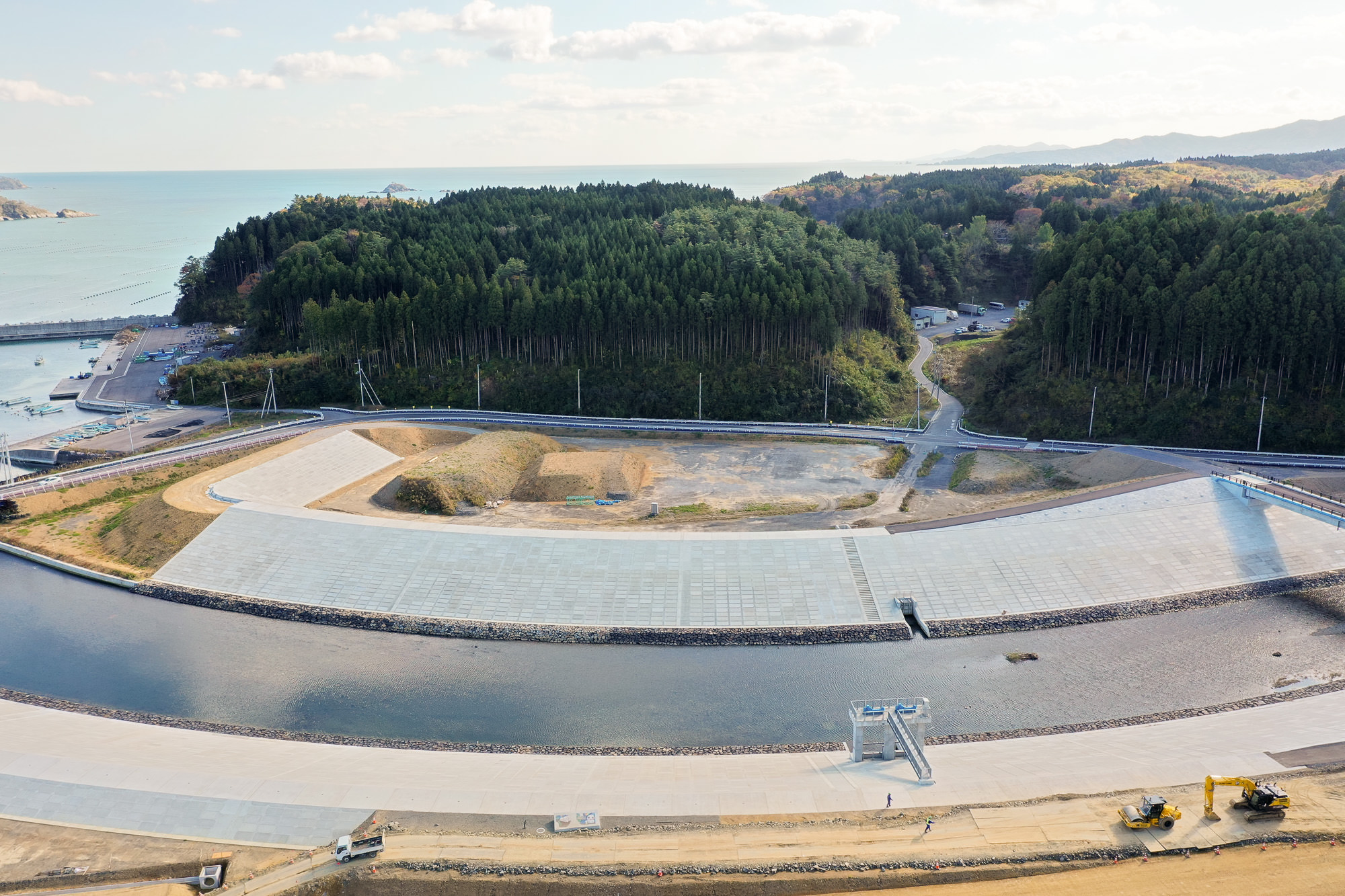 湾に面した山とその手前にある川の中洲のような地形、周囲を囲む道路や小さな建物が見える広角の写真