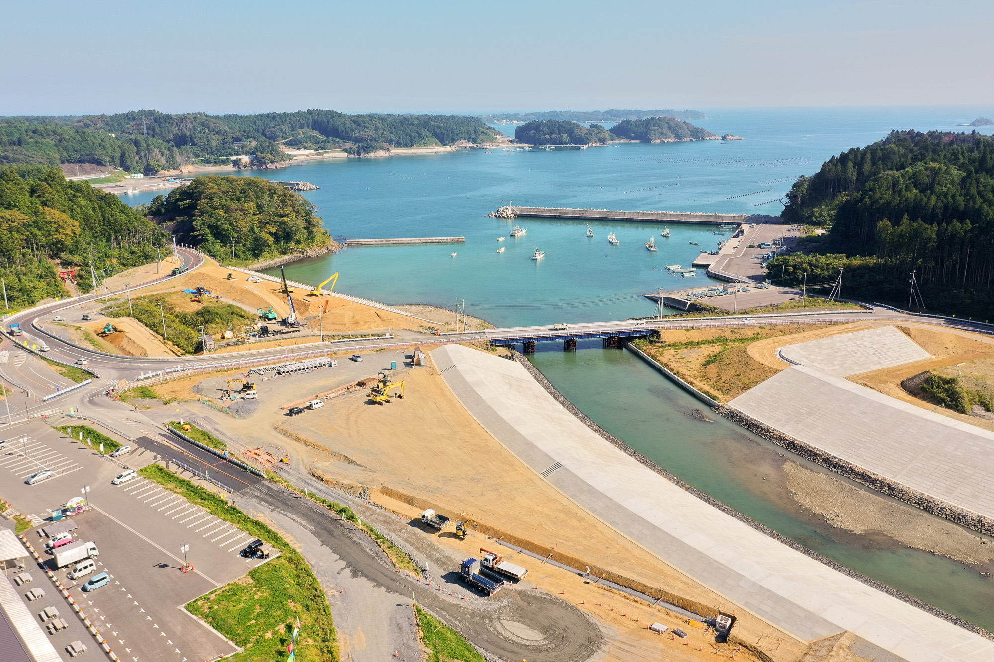 海に向かって広がる港と、川沿いで進行中の防潮堤の工事現場が同時に写されている写真