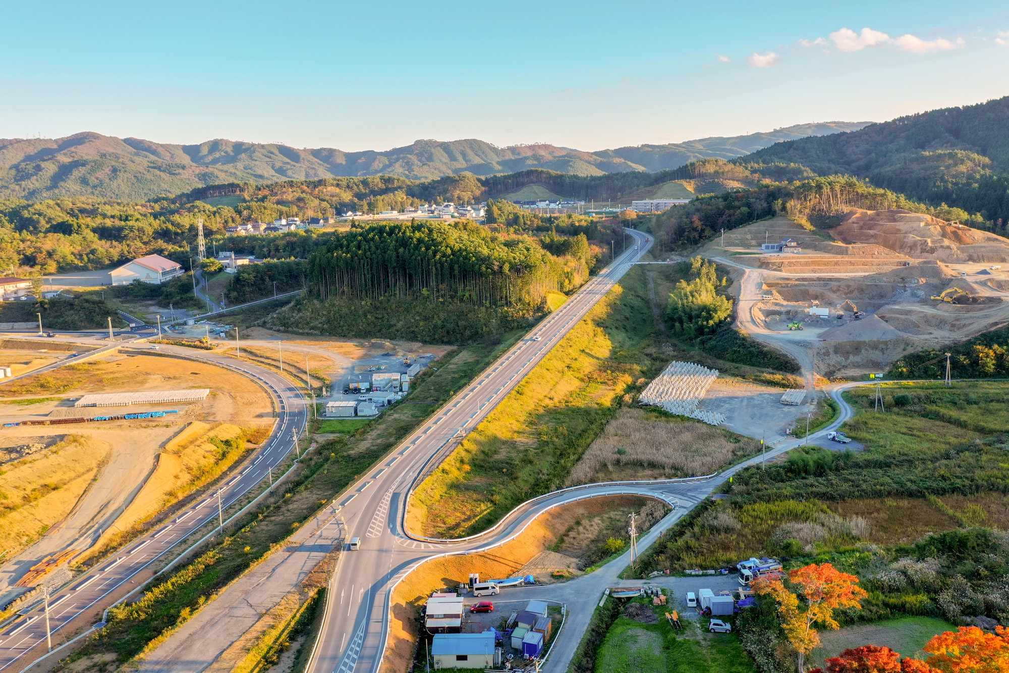 山のふもとに広がる造成地に道路や建設機材が配置され、奥には住宅地や学校のような建物が見える開発地域の写真