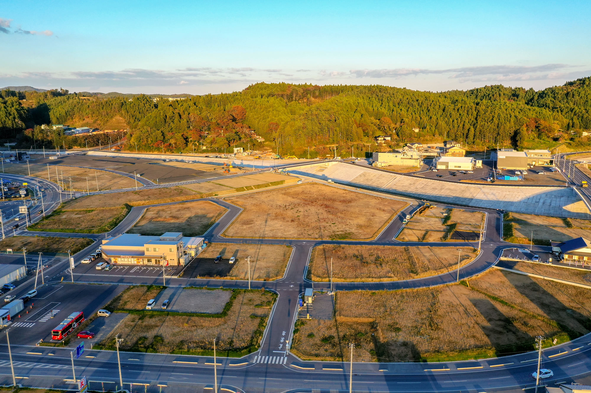 広く整地された六角形状の造成地と建設中の建物、背後の緑に覆われた山を中心に、整備が進む町の中心部を撮影した写真