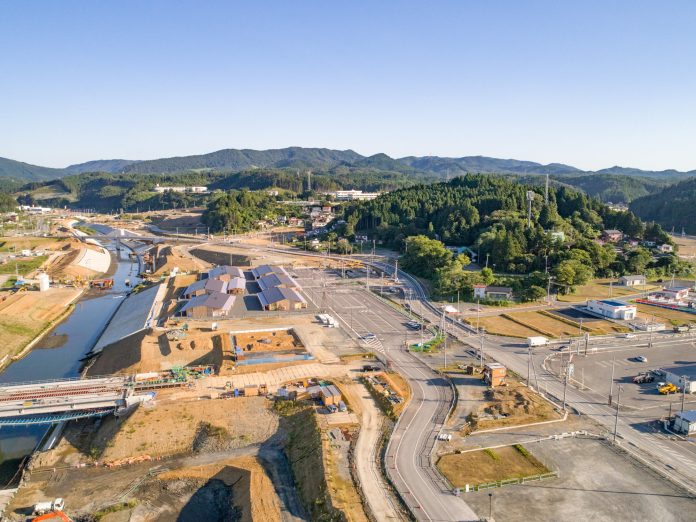 左側に川が流れ、周囲を山々に囲まれた広大な敷地で、建設作業が進められている様子を上空から捉えた工事現場の写真