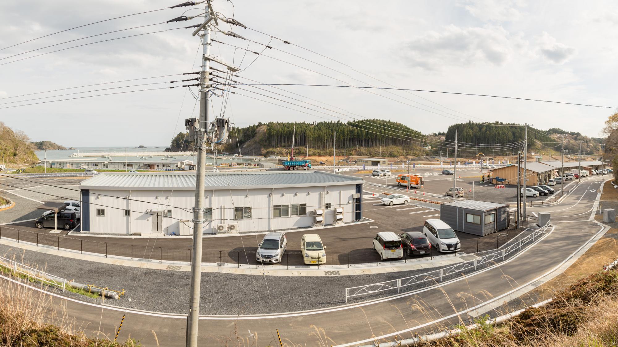 中央には白い屋根の平屋建ての建物があり、その前には数台の車が整然と駐車され全体に電柱と電線が張り巡らされており、インフラ設備が整ってきた様子を写した写真