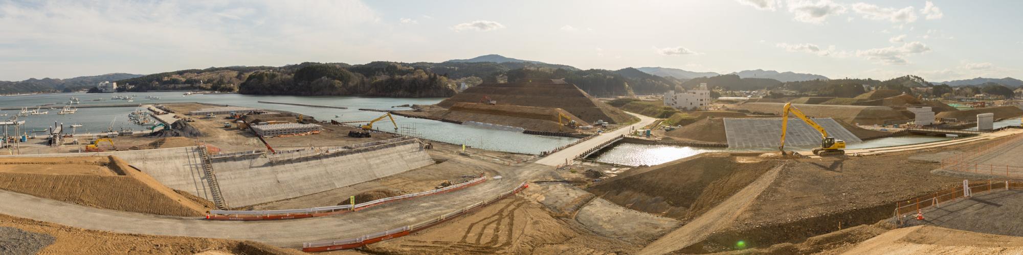 画面の中央には水路が通っており、その周囲には土砂やコンクリートでできた構造物が配置された海岸沿いに広がる大規模な建設現場の写真