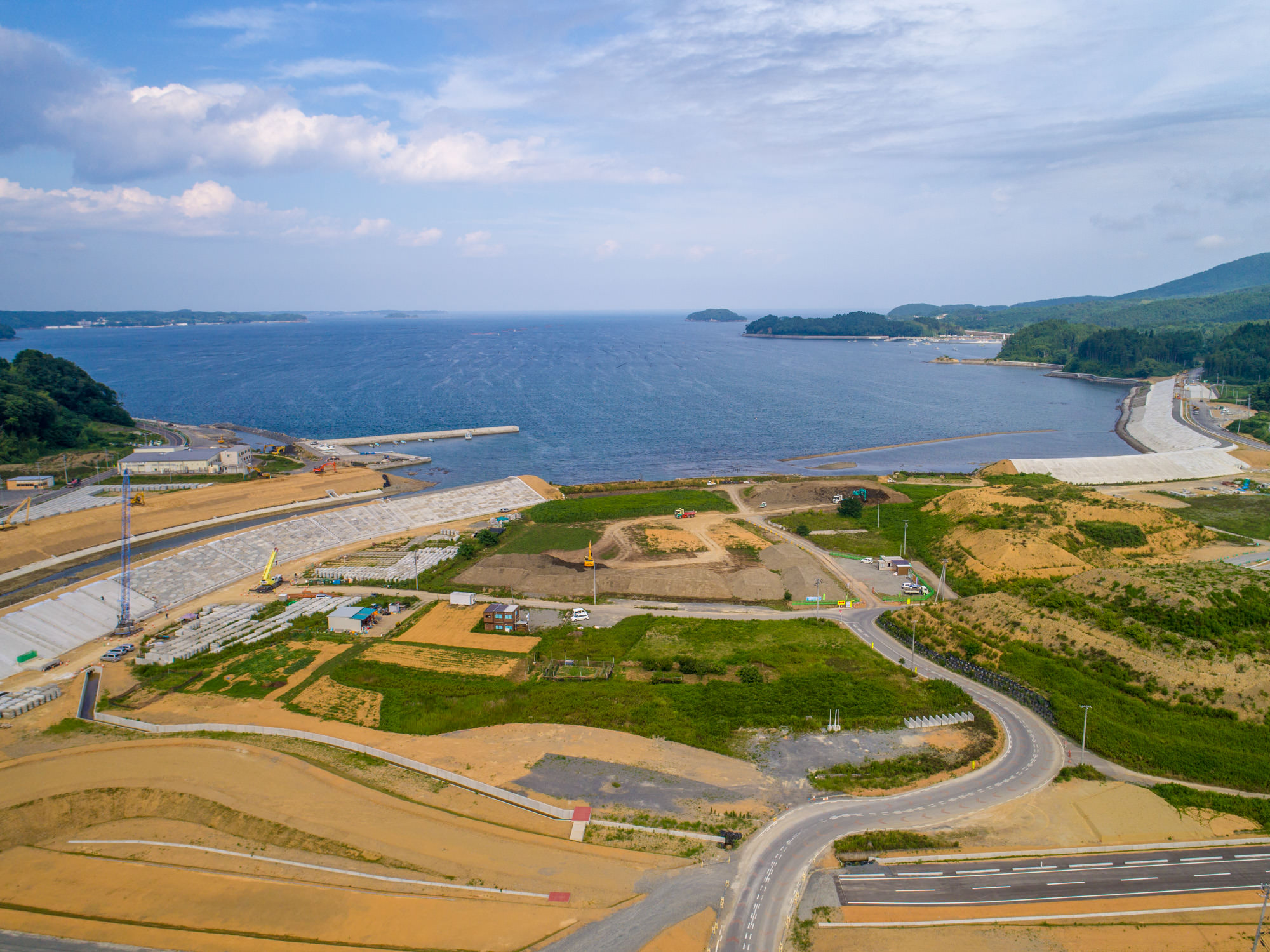 海に面した広い土地に道路や緑地が広がり、一部が工事中で、海には防波堤や桟橋のような構造物が突き出している様子を写した沿岸開発の写真