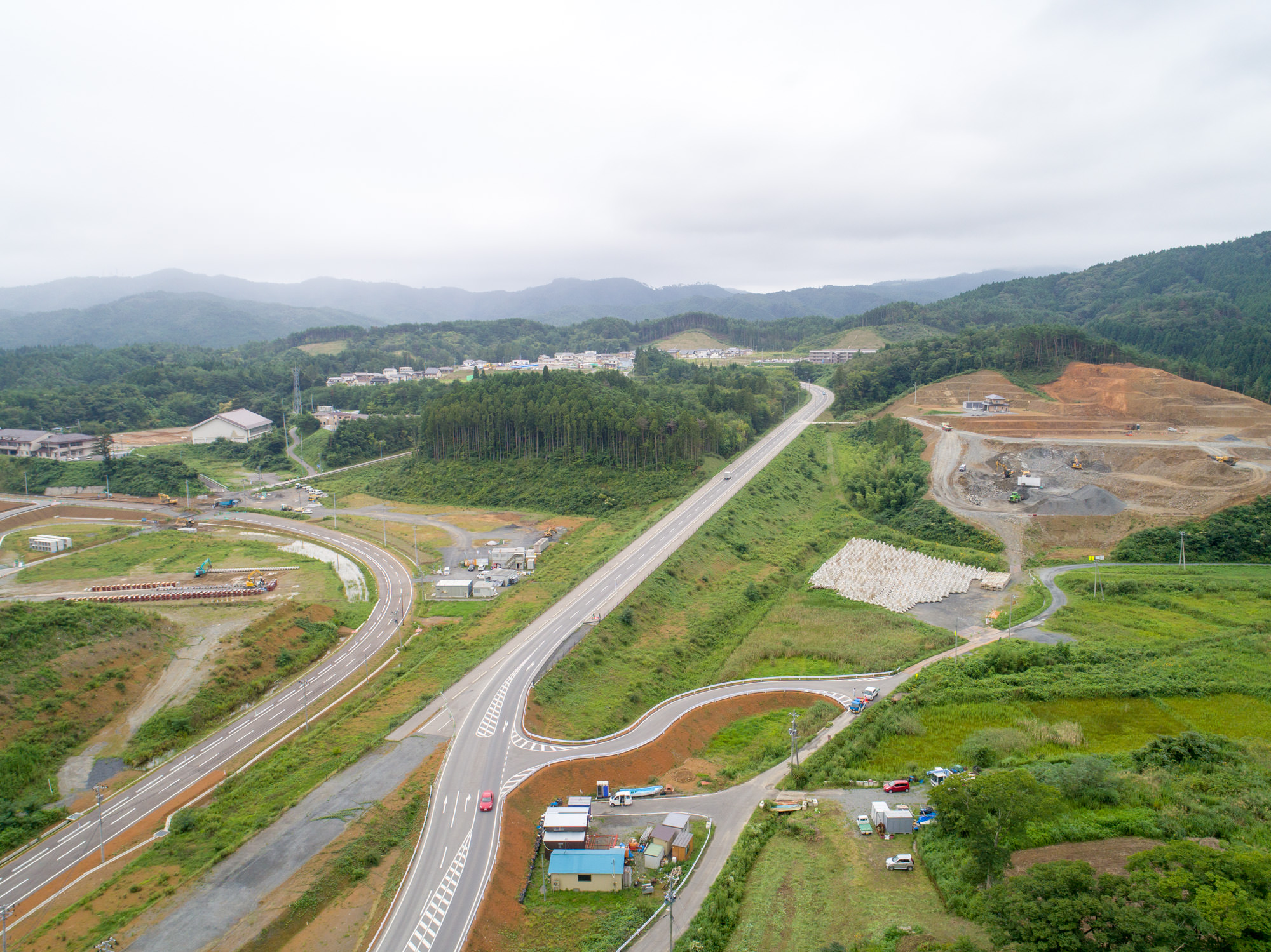 山あいの道路が新しく整備され、左手には工事中の造成地や住宅地が見え、右手奥には大規模な造成工事が進んでいる様子の写真