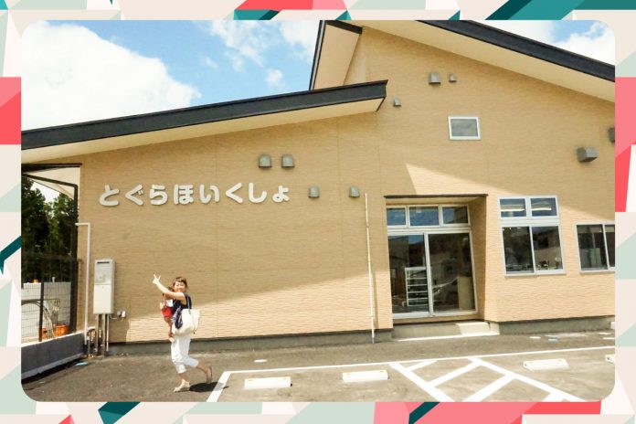 「とぐらほいくしょ」と書かれたベージュ色の外壁を持つ建物の前に、小さな子供を抱っこした女性が建物を指さして立っている写真の周りにカラフルな縁取りがされている画像