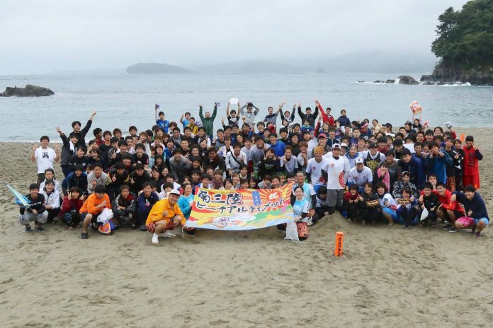 青い海と白い砂浜を背景に、「南三陸ビーチアスティメット」の横断幕を中央の方々が持っており、大勢の参加者が集まった集合写真