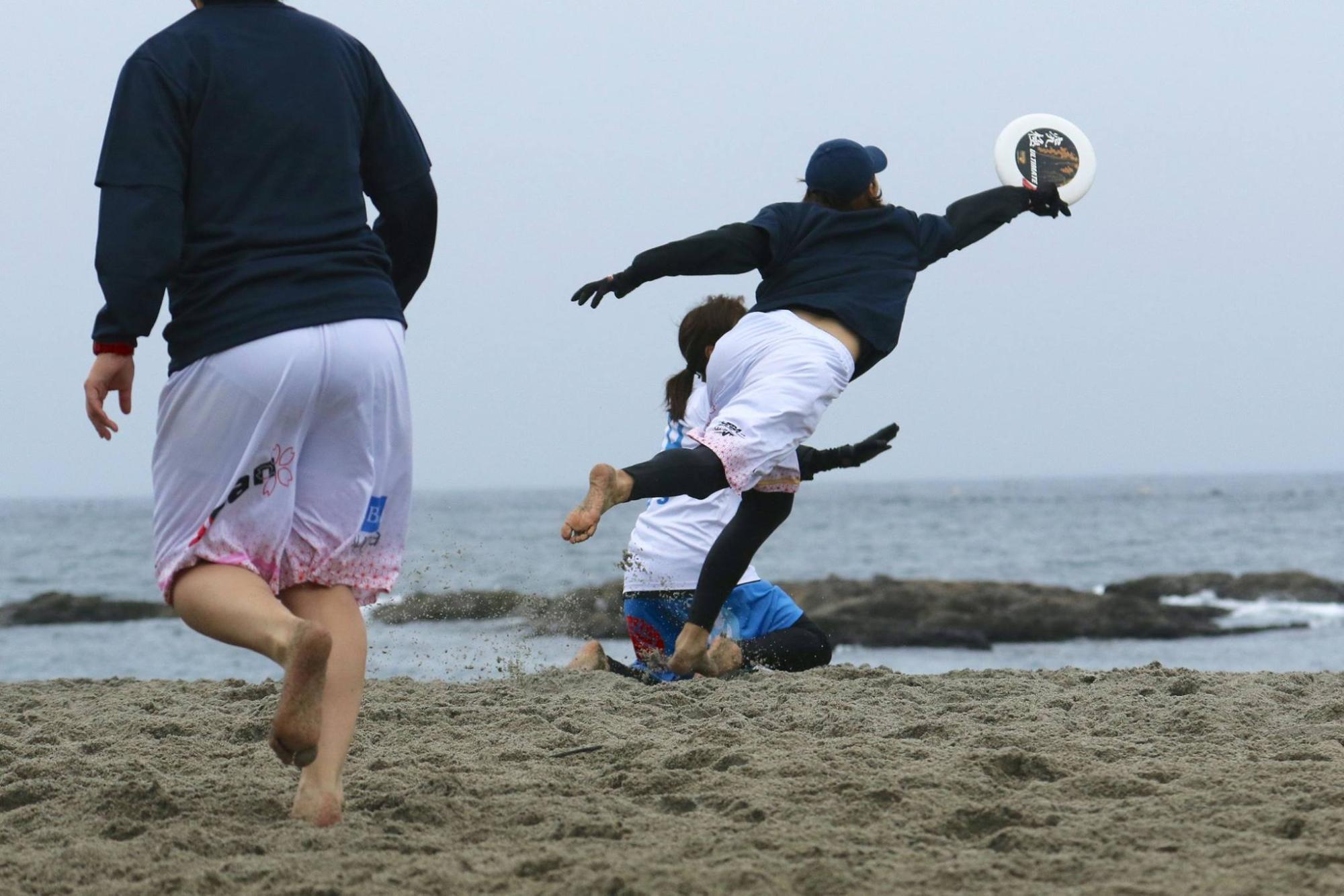 円盤のフリスピーをダイブして取ろうとしている人の後ろ姿を写した写真