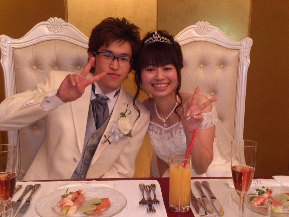 金屏風が設置された結婚式の披露宴で、白いタキシードの男性と白いドレスを着た花嫁が仲良く並び、ピースサインをして笑っている写真